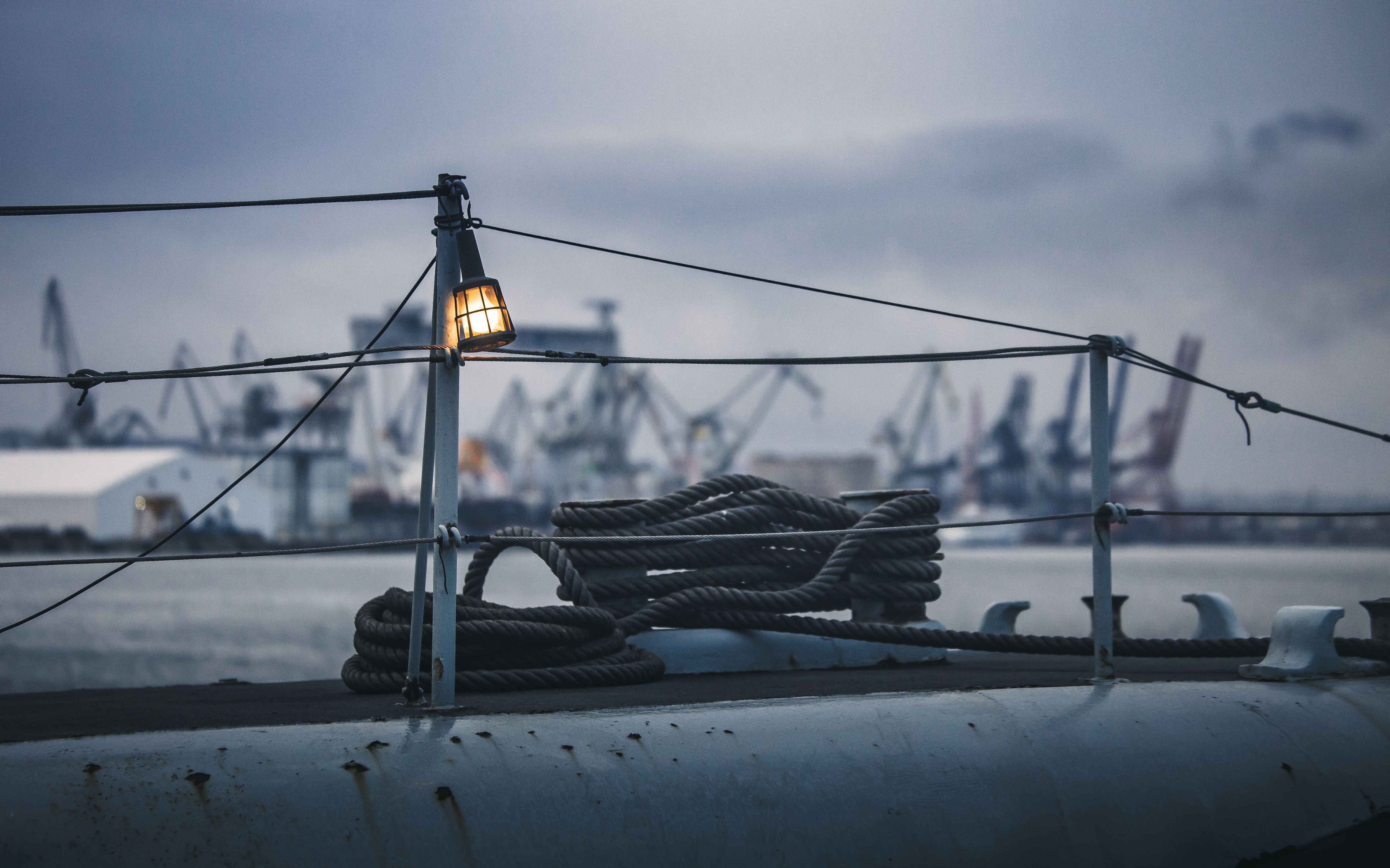 A serene view of Gdynia's industrial harbor at twilight, with ropes and cranes under a cloudy sky.