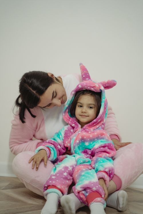 Free A mother and daughter sitting indoors, both in cozy, colorful unicorn pajamas. Stock Photo