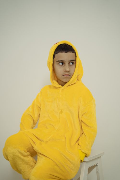 Free Young boy in a yellow onesie poses on a stool, hands in pockets, against a white studio backdrop. Stock Photo