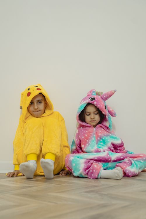 Free Two children sitting in brightly colored animal onesies on a hardwood floor. Stock Photo