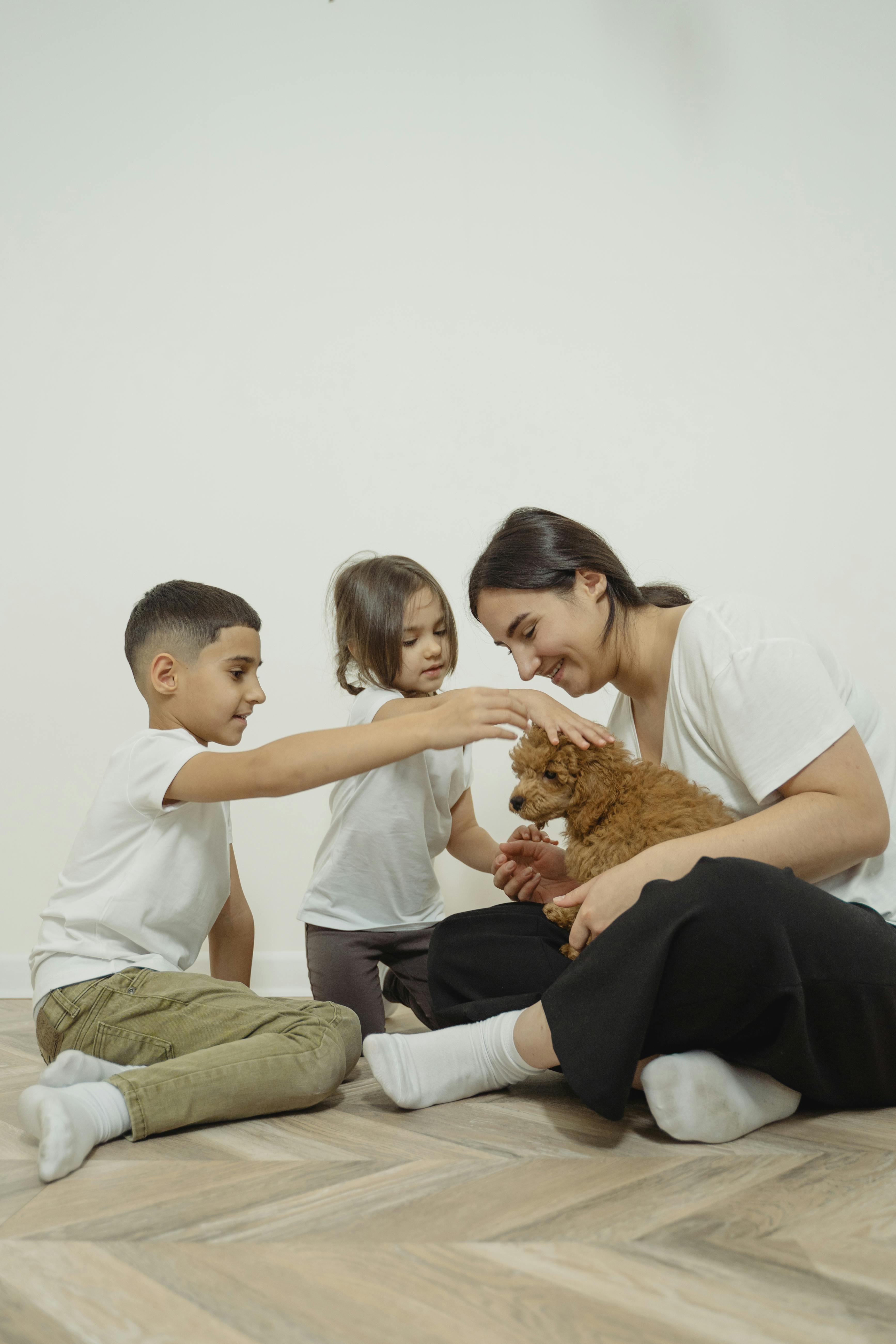 母亲和两个孩子坐在室内的木地板上，与小狗共度欢乐时光