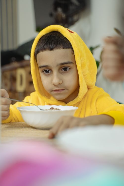 Free A young boy wearing a yellow hoodie enjoys breakfast cereal indoors. Stock Photo