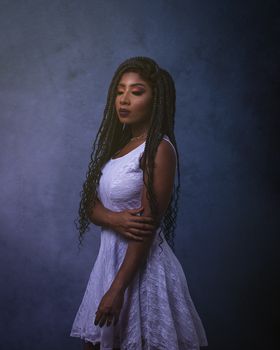 Studio portrait of a woman in a white dress, styled with braids against a dark background.