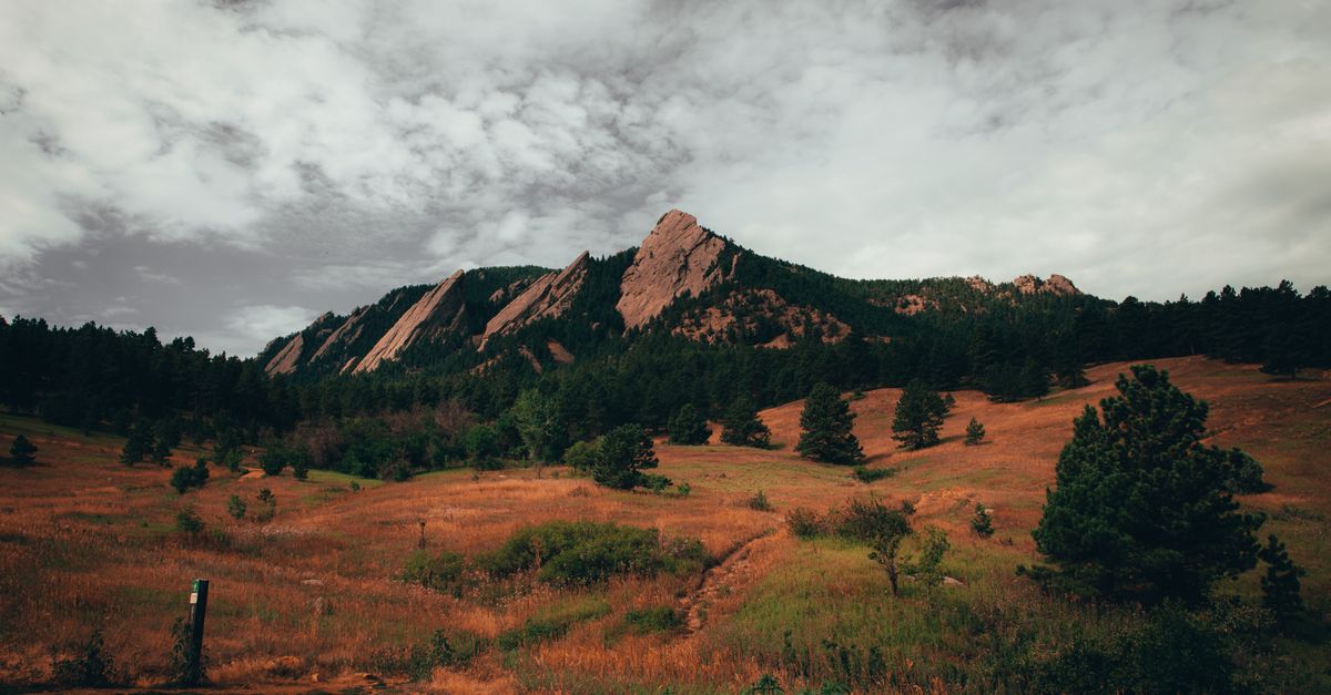 A dramatic view of the Flatirons rock formation under a cloudy sky in Boulder, Colorado.