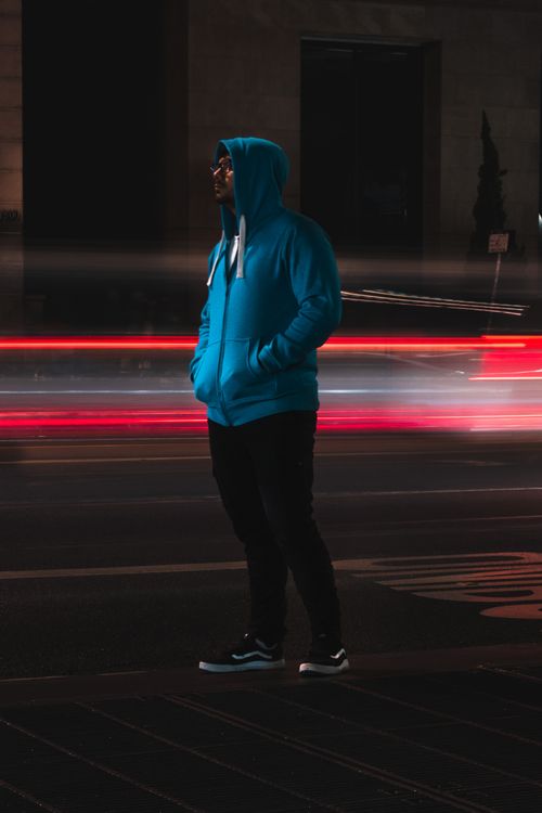 Free Side view of young man in casual outfit keeping hands in pockets waiting for transport standing on bus stop on empty city road Stock Photo