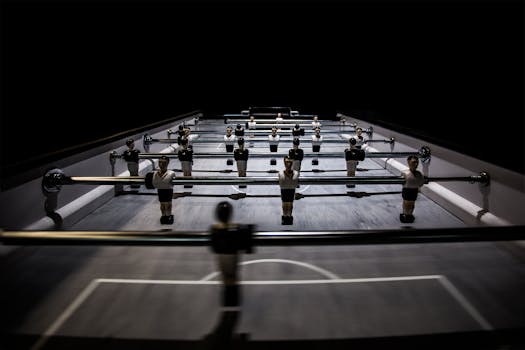 A close-up view of a foosball table under dramatic lighting, highlighting players and game dynamics.