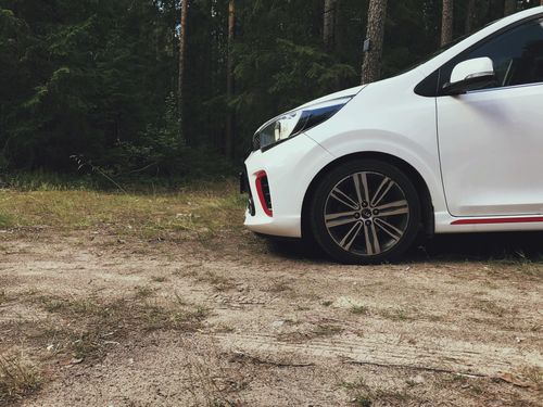 Free Side view of a white compact car in a forest, ideal for travel themes and ads. Stock Photo