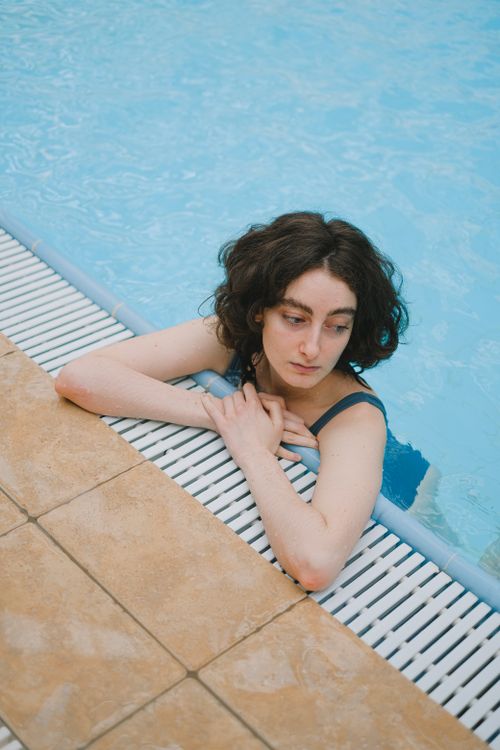 Free Woman relaxing at the edge of a swimming pool, enjoying leisure time outdoors. Stock Photo