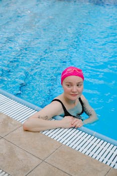 A young woman relaxing in a swimming pool wearing a pink swim cap and black swimsuit.