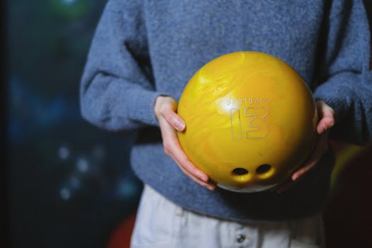 Close-up of a person holding a yellow bowling ball indoors, highlighting leisure and recreation.