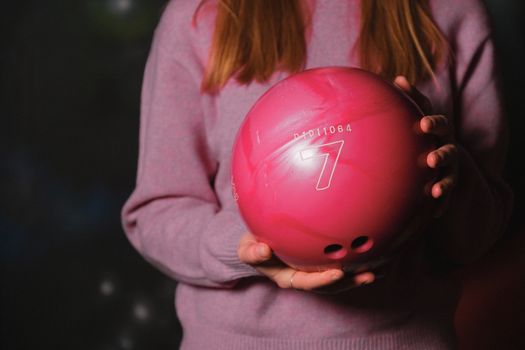 A woman holding a pink bowling ball with number 7, ready for a game indoors.