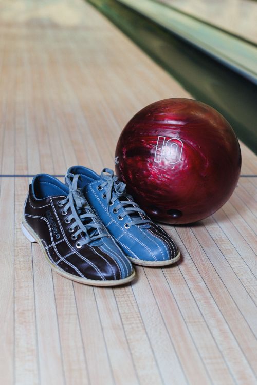 Free A pair of colorful bowling shoes beside a maroon bowling ball on a wooden lane. Stock Photo