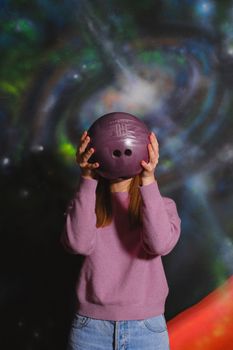 一名女子以紫色保龄球遮住脸，背景是色彩缤纷的宇宙