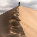 Person in Black Jacket Walking on Brown Sand Under White Cloudy Sky