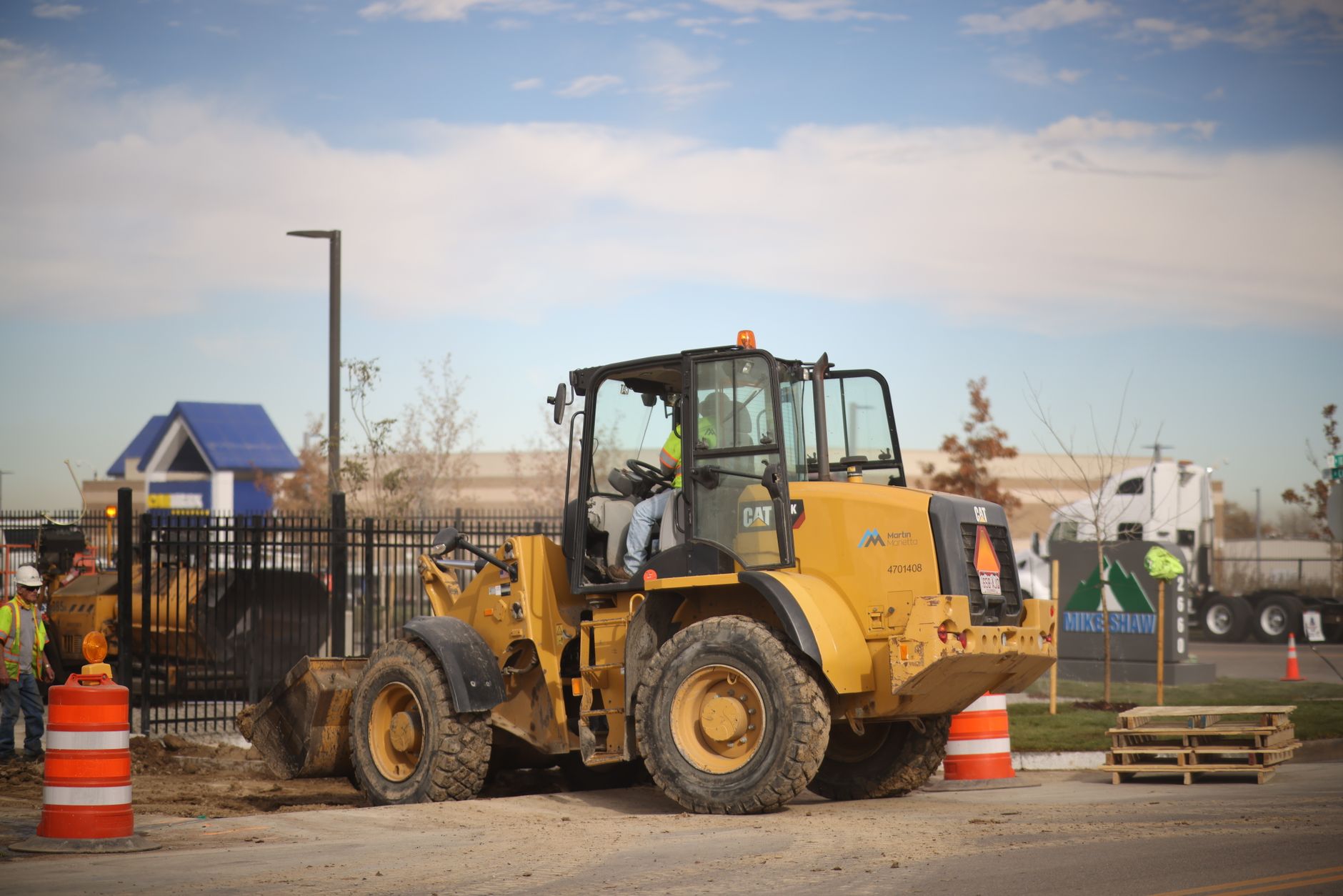 A bulldozer operating at a roadside construction site with workers and machinery in the background.