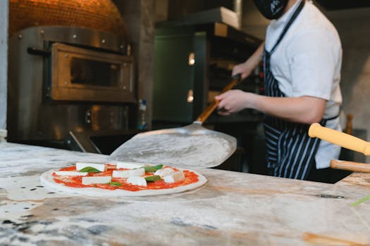 Chef preparing a fresh pizza in a pizzeria kitchen with traditional oven.