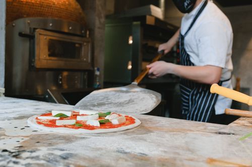 Free Chef preparing a fresh pizza in a pizzeria kitchen with traditional oven. Stock Photo