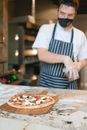 Man in White and Black Stripe Apron Holding Pizza