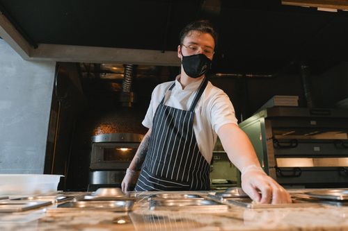 Free A baker wearing a face mask and apron works in an industrial kitchen setting. Stock Photo