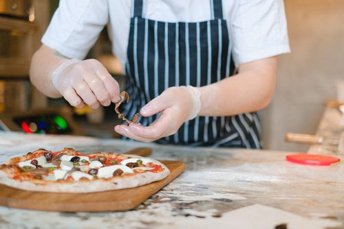 Free A chef adds toppings to a freshly prepared pizza in a cozy kitchen setting. Stock Photo