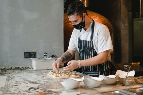 Free A chef wearing a face mask intricately prepares pizza dough in a professional kitchen. Stock Photo