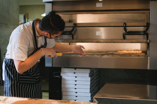Free A chef in an apron prepares pizza in a commercial kitchen oven. Stock Photo