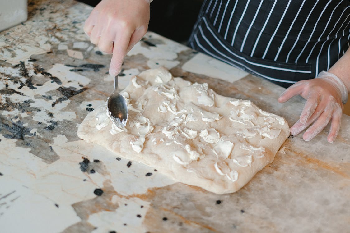 chef spreading cheese on pizza dough on a surface