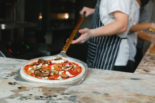 Free Chef placing fresh vegetable pizza into the oven in a pizzeria kitchen. Stock Photo