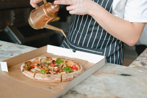 Free Close-up of chef adding olive oil to a fresh pizza in a pizzeria kitchen. Stock Photo