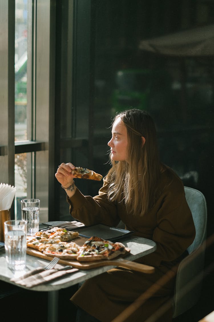 Woman Eating Pizza Sitting By Restaurant Window