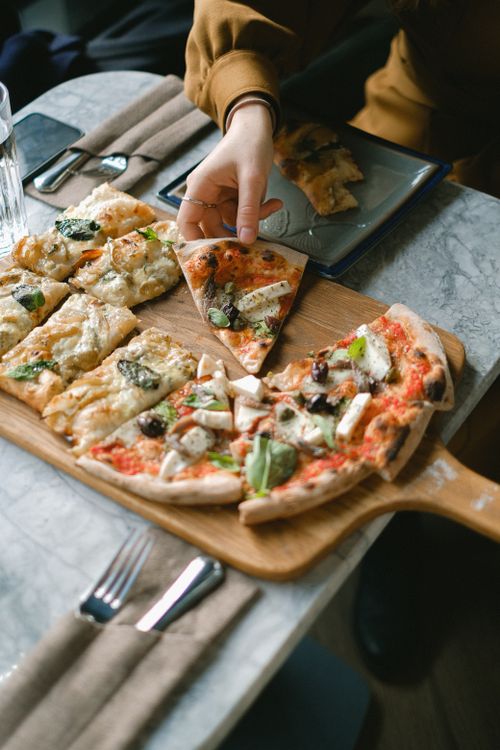 Free A hand reaching for a slice of fresh pizza on a wooden board, ideal for restaurant themes. Stock Photo