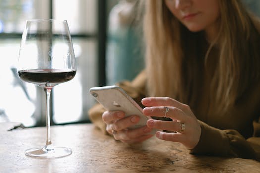A woman with long hair relaxes with a smartphone and wine glass in a cozy restaurant setting.