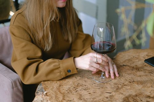 Free A woman relaxes indoors, holding a glass of red wine at a rustic wooden table. Stock Photo