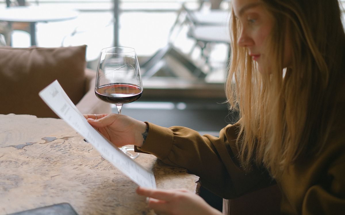 A woman reads a menu while holding a glass of red wine at a restaurant.