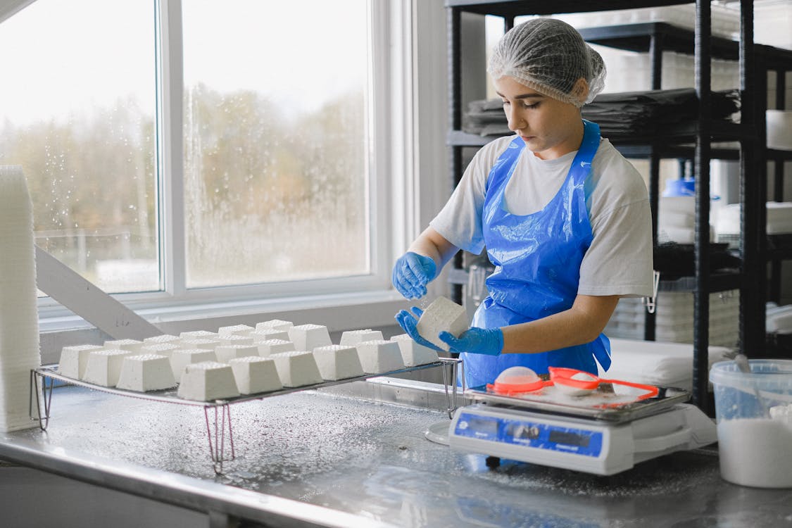 A woman in uniform, gloves, and head cover, working in a food processing plant