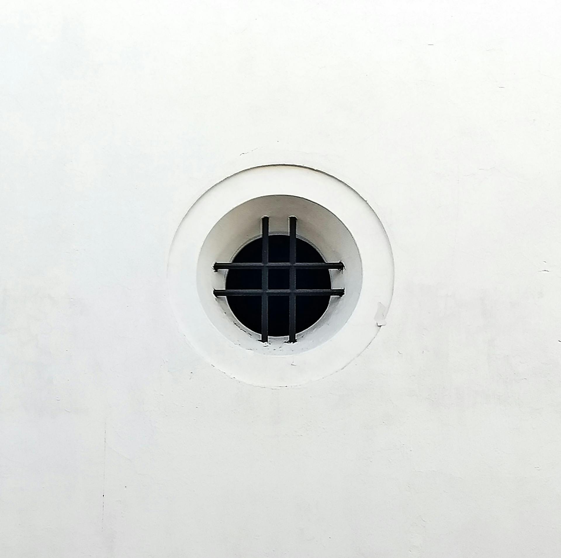 Minimalist white wall featuring a circular vent with decorative iron bars, creating a modern design element.