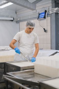 一名男子在乳制品厂里穿着防护装备，拿着一把勺子