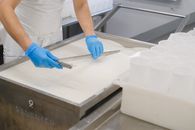 A worker in blue gloves cuts curds in a cheese factory using specialized tools.