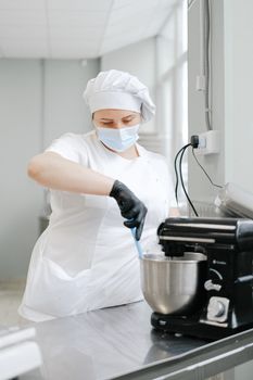 在商业厨房里，一名戴着防护装备的厨师正用立式搅拌机混合食材