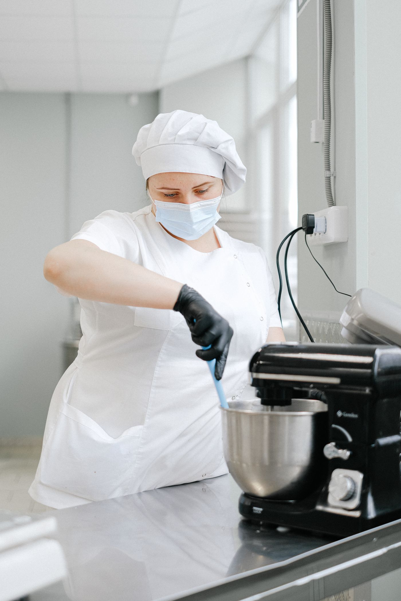 Baker operating a professional stand mixer with a stainless steel mixing bowl