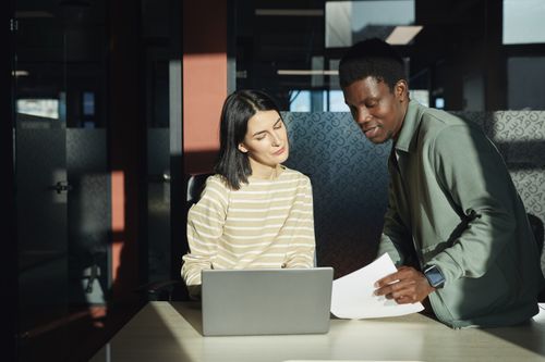 Free Two professionals discussing work over a laptop in a bright, modern office setting. Stock Photo