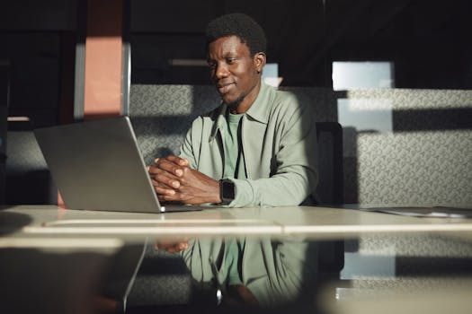 African American businessman focused on a laptop in a modern office setting, reflecting productivity and technology.