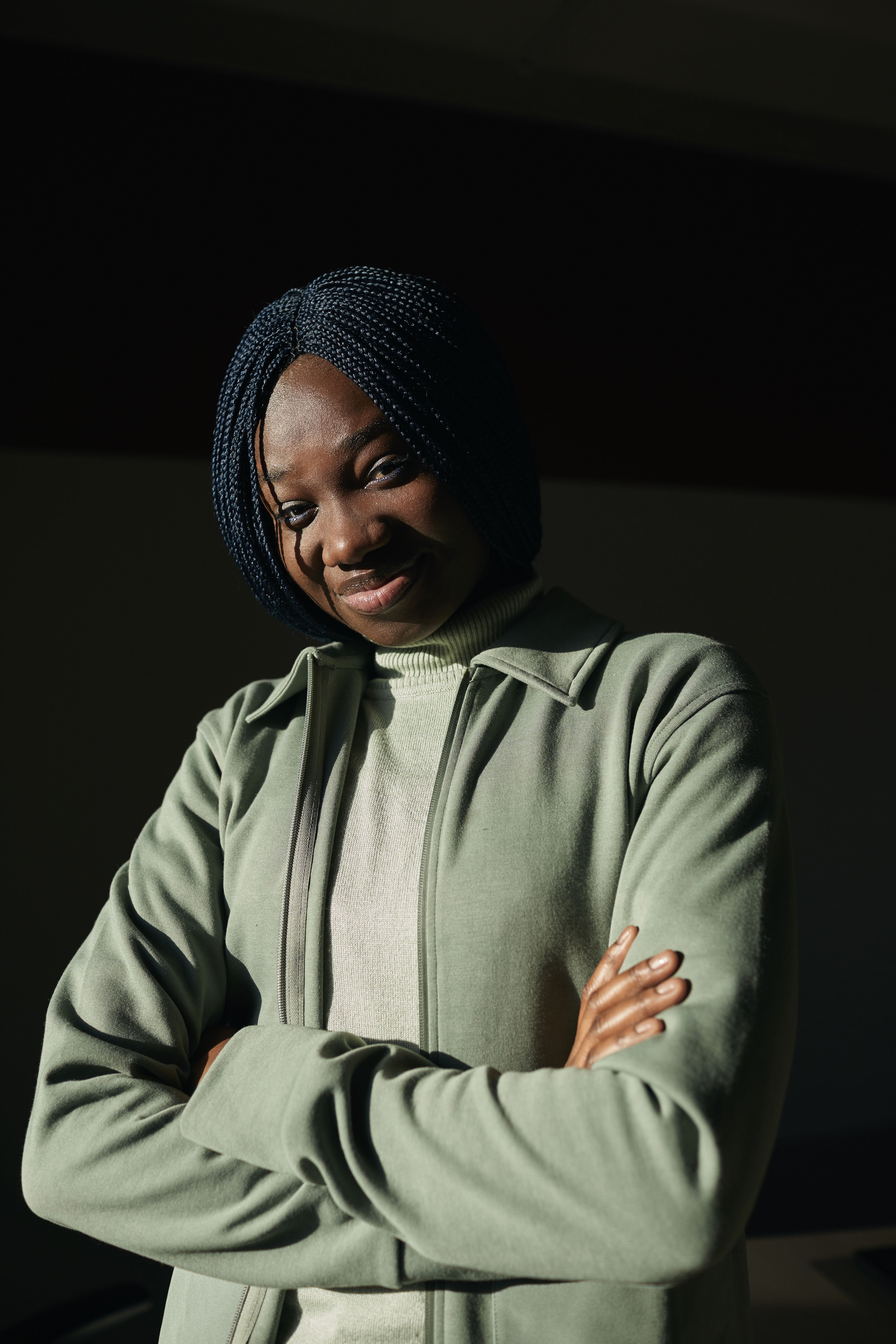 Portrait of a woman with braided hair in a casual green jacket, looking confidently.