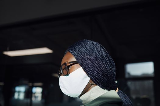 Side view of a stylish person with braided hair and eyeglasses wearing a face mask indoors.