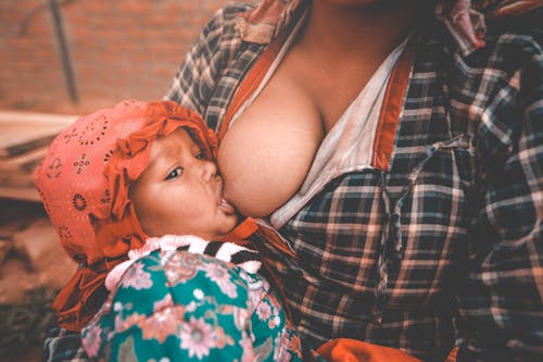 Ethnic young mother breastfeeding baby in village