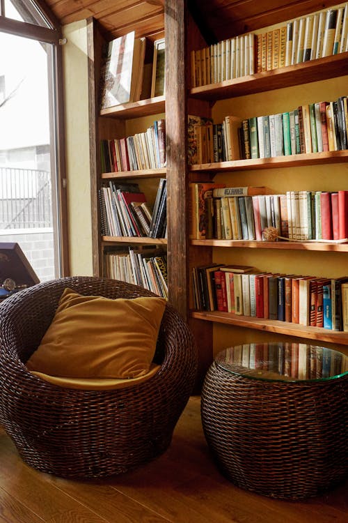 Wicker Chair and Table Beside Books on Wooden Shelves