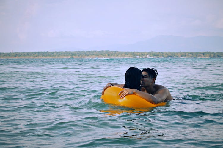 Man Kissing A Woman In An Inflatable Floater On The Beach