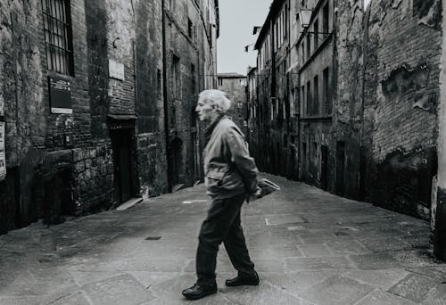 Free Man in Gray Jacket Walking in an Alley in Grayscale Photography Stock Photo