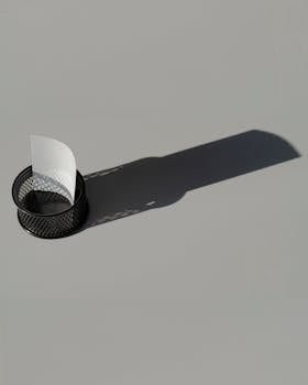 A minimalistic wire mesh paper holder casting a long shadow on a smooth surface.