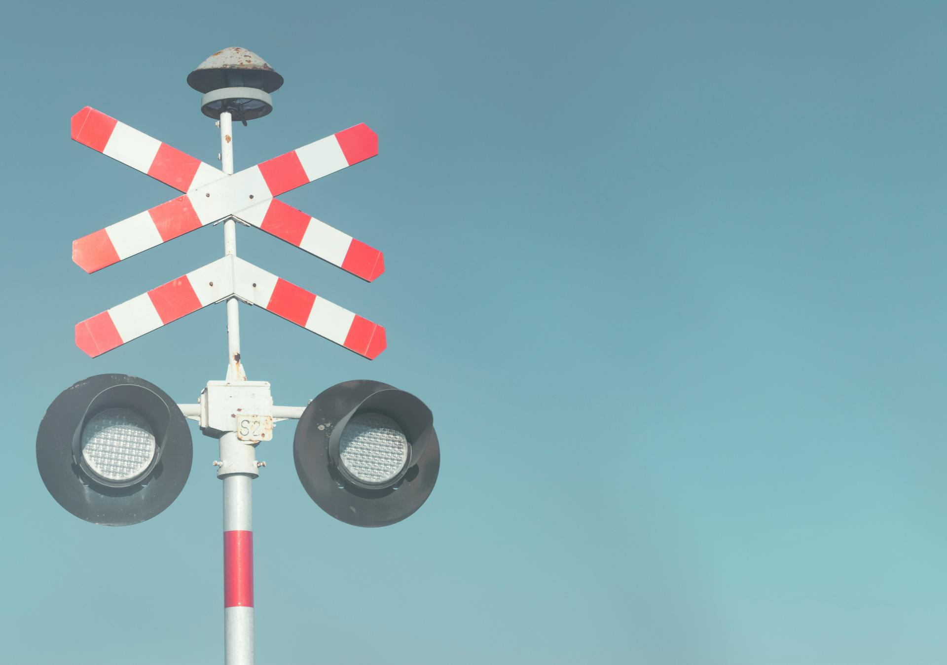 Bright railroad crossing sign with lights against a blue sky.